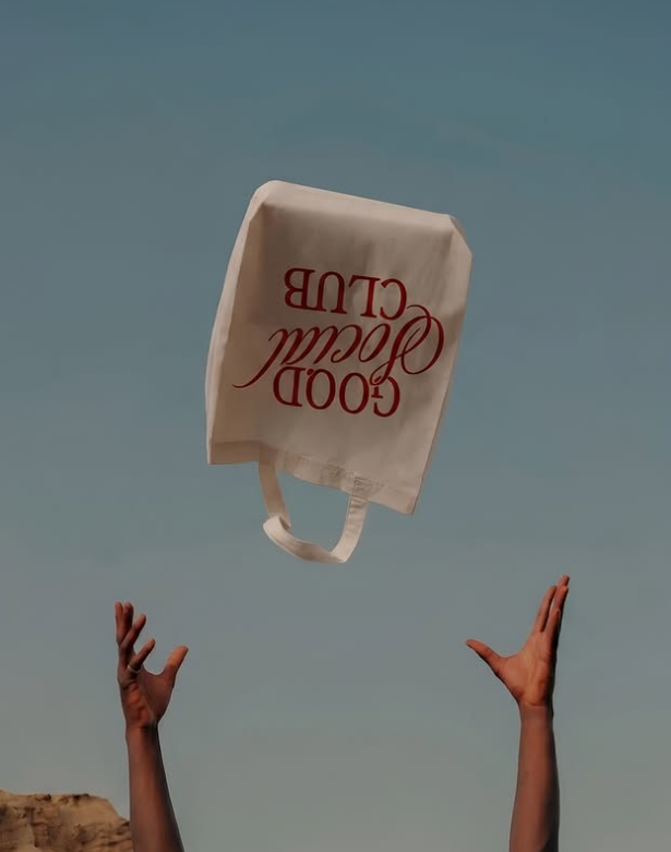 Good Social Club tote bag tossed into a clear blue sky